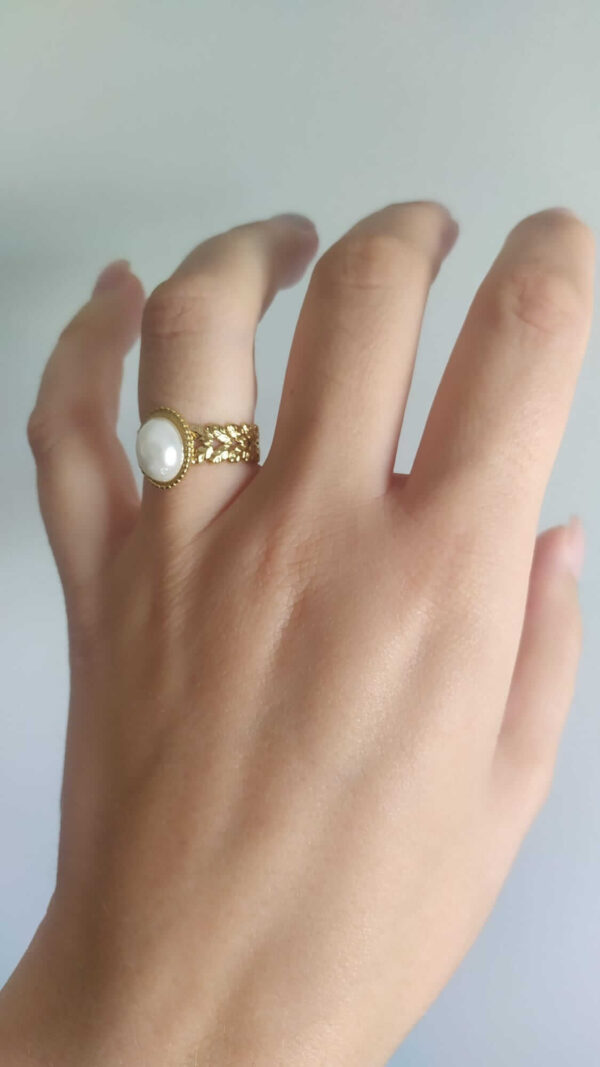 Anel ajustável em aço com pérola no centro e laterais com folhas trabalhadas, dourado